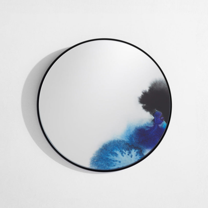 A round wall mirror with a thin black frame and blue and black ink washes in one corner