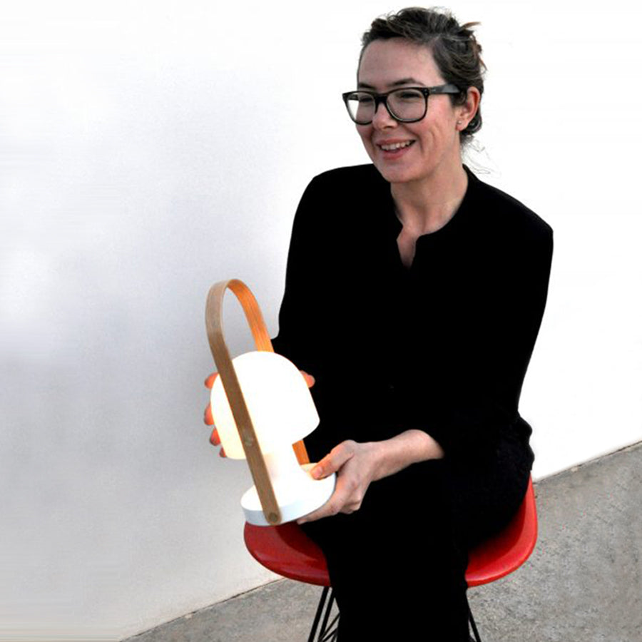 A person seated on a red chair holds a glowing white portable lamp with a curved wooden handle