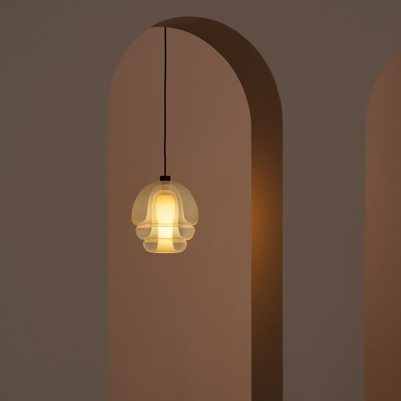 A glowing pendant of layered translucent glass on a black cord, hanging in a tall arched doorway
