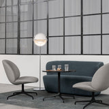 A floor lamp with a white round shade beside a blue-grey sofa, small round table and two grey swivel chairs