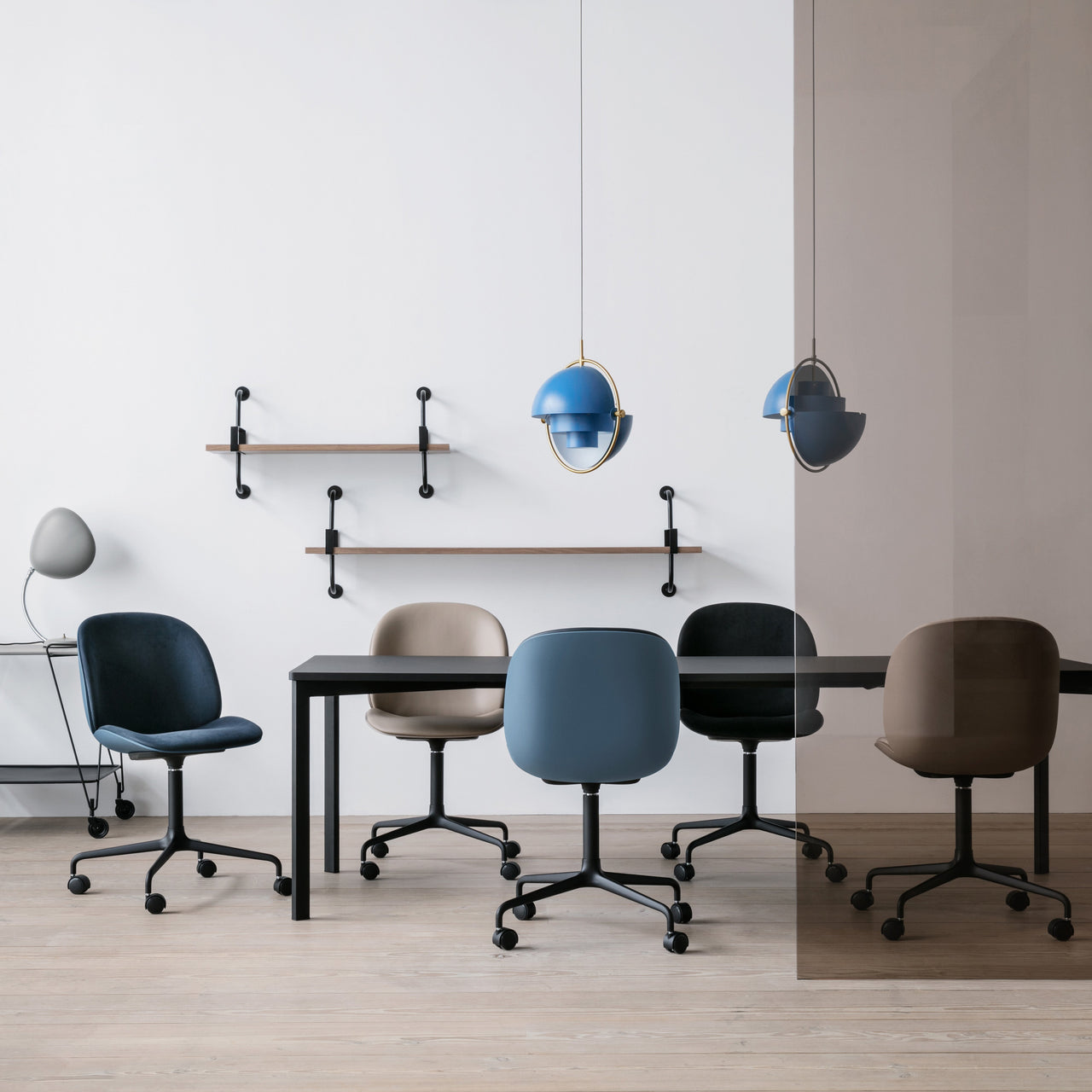 A blue pendant light with brass ring hangs over a black table and five swivel chairs on casters