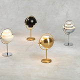 Four table lamps with tilting half-dome shades in brass, black, cream and chrome on a grey surface