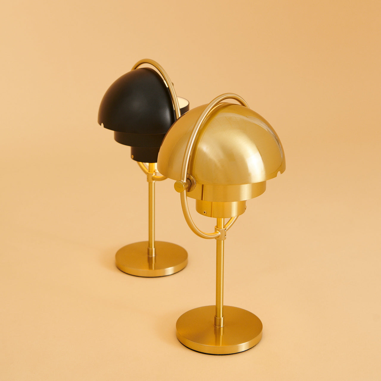 Two table lamps with domed shades on round brass bases, one polished brass and one matte black