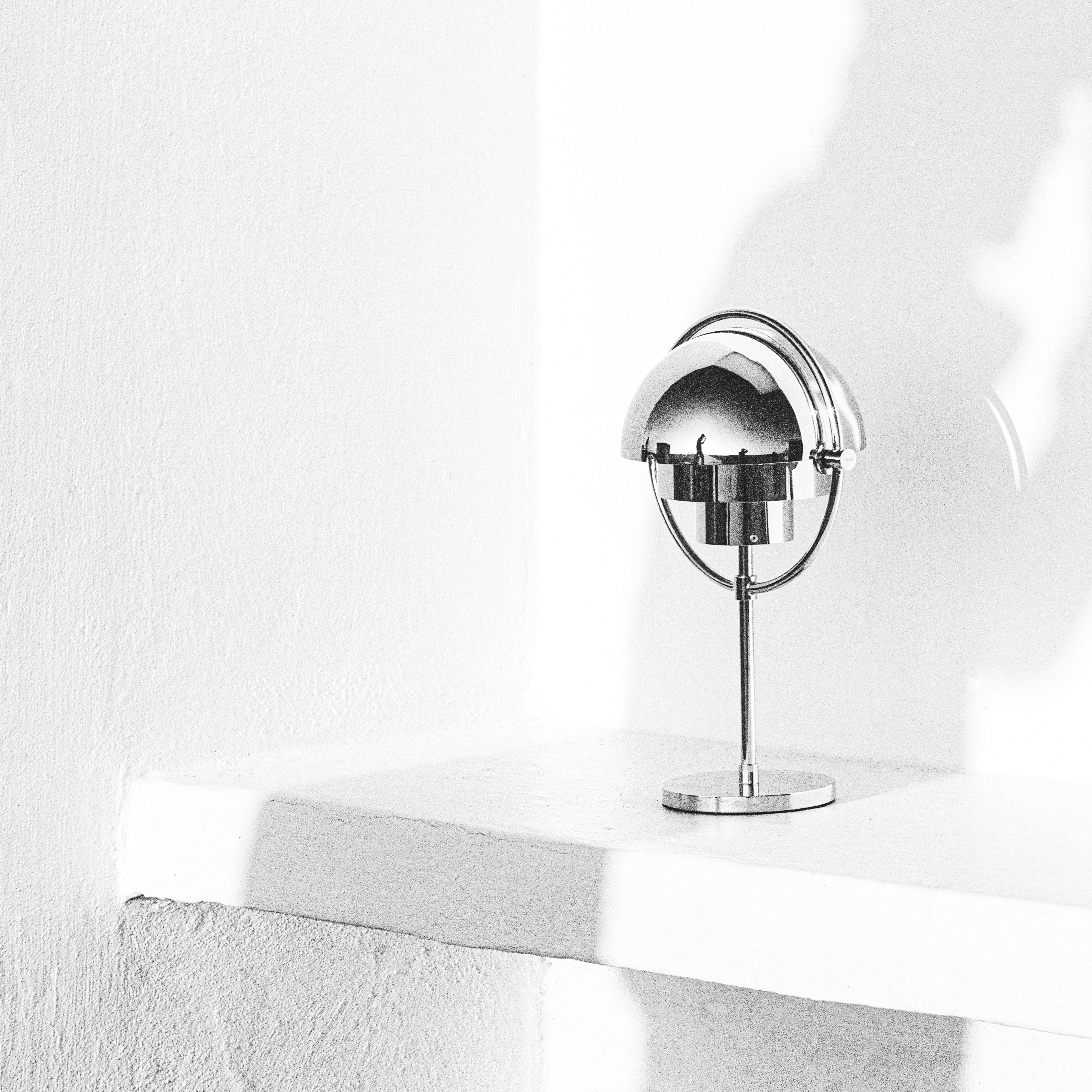 A small chrome table lamp with a half-dome shade on a thin stem, on a white ledge