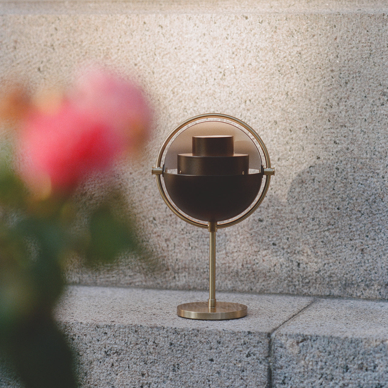 A small brass table lamp with a dark half-dome shade in a ring, on a granite step