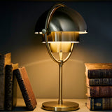 A brass table lamp with a half-dome shade on a curved arm, lit, between old leather-bound books