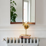 A polished brass table lamp with a round pivoting shade sits on two books beneath a wall mirror