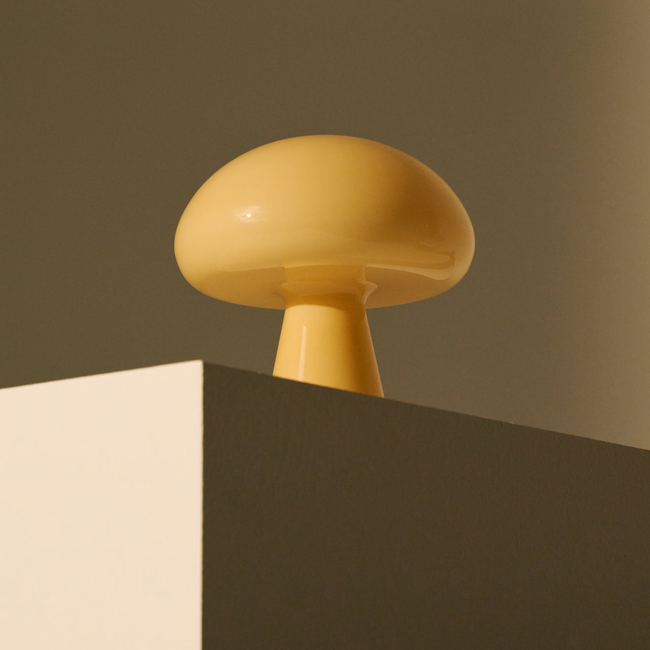 A glossy pale yellow glass table lamp shaped like a mushroom, set on the corner of a block