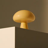 A glossy pale yellow glass table lamp shaped like a mushroom, set on the corner of a block