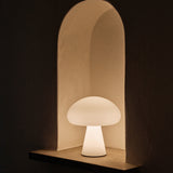 A glowing white mushroom-shaped lamp sits in an arched plaster wall niche in a dark room