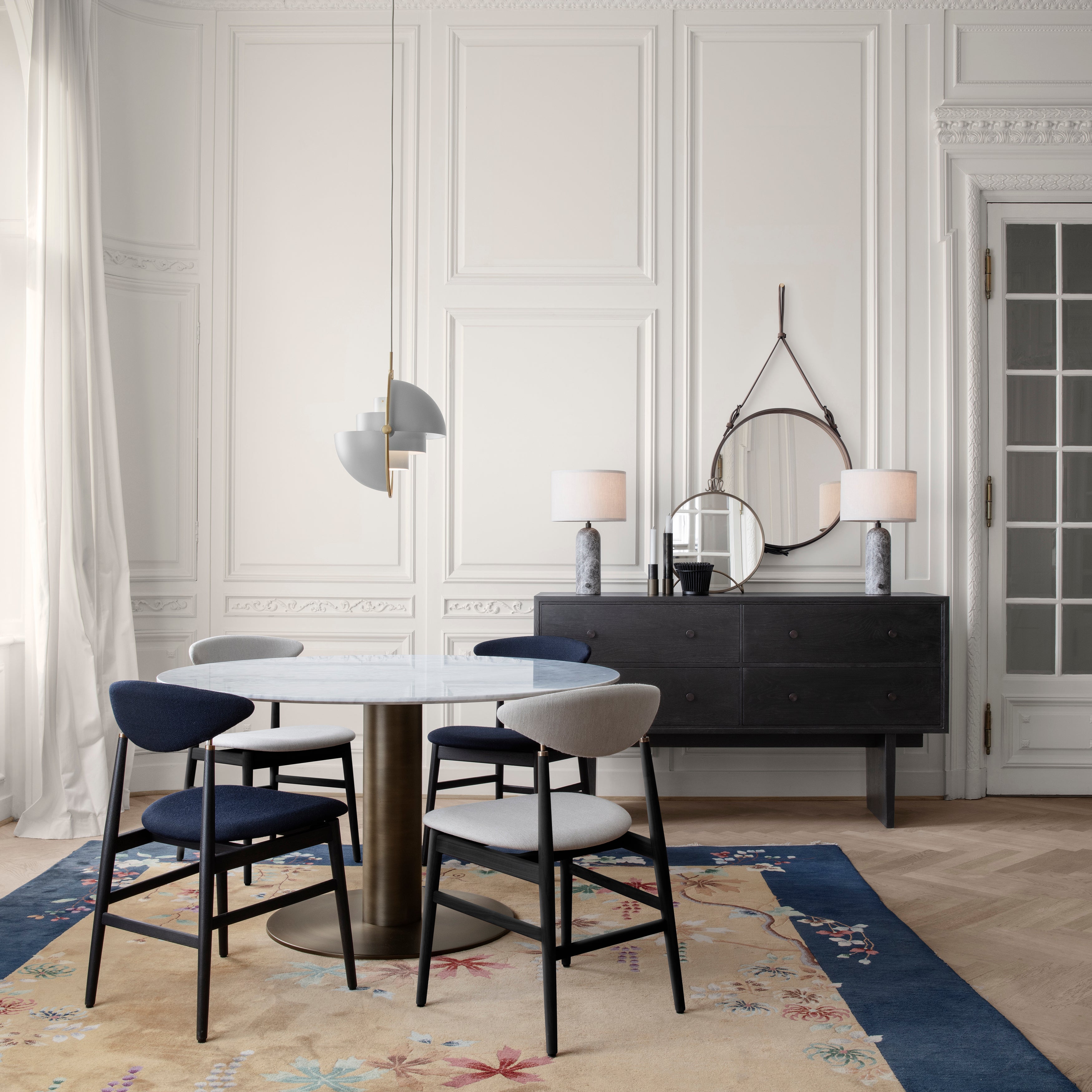 A dark wood sideboard with drawers and two marble lamps, beside a round dining table with four chairs
