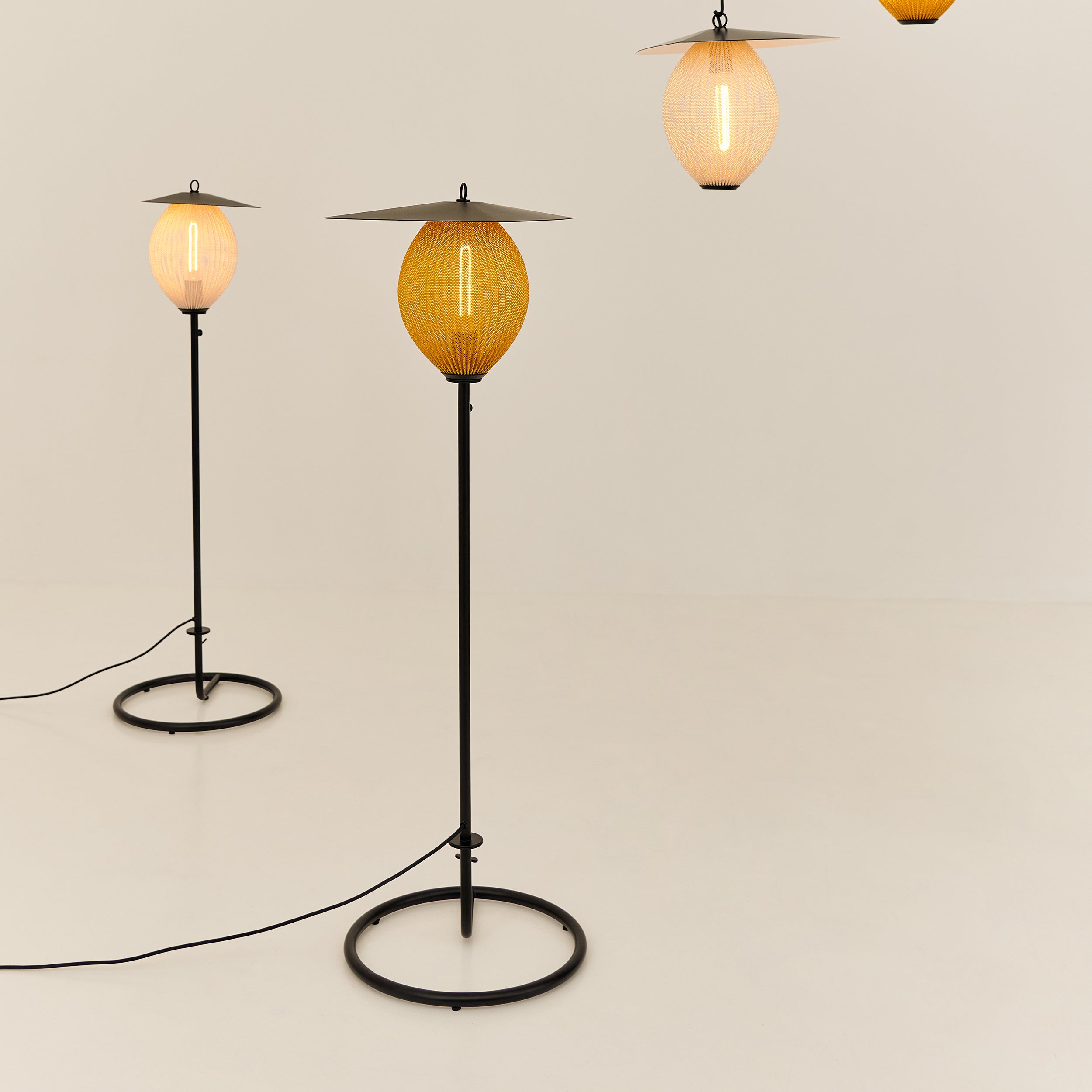 Two floor lamps with glowing amber and cream oval shades on thin black stems and round bases, with pendants above