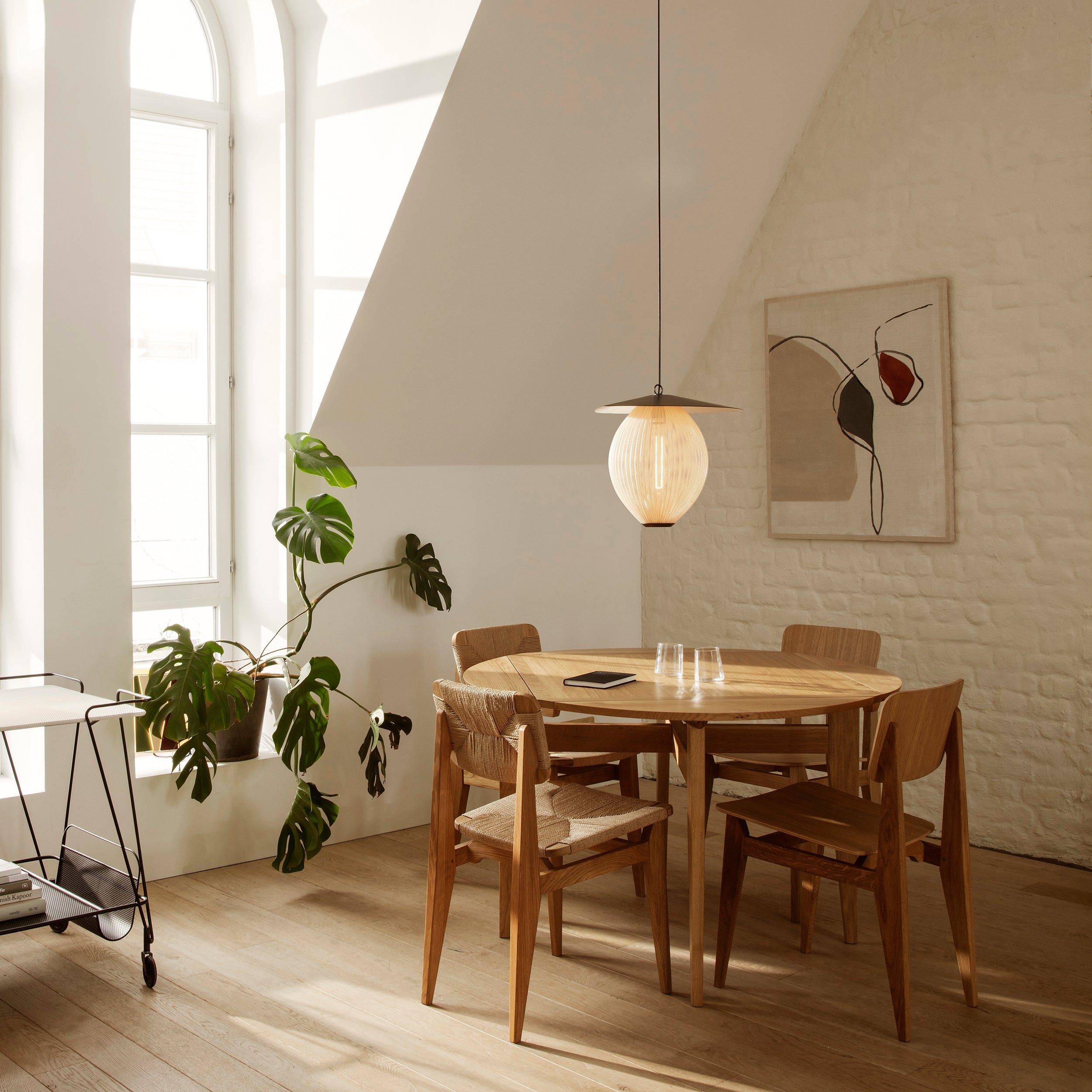 A glowing ribbed globe pendant with a flat conical top hangs above a round wooden dining table and chairs