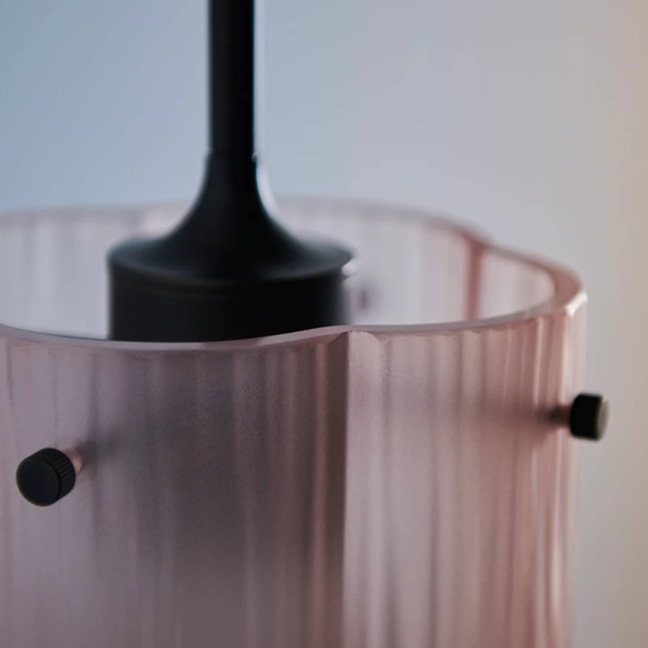 Close-up of a pale pink ribbed glass pendant shade with a wavy rim, black fitting and black knobs