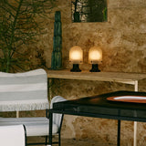 Two small glowing domed lamps with black bases on a narrow table against a rough stone wall