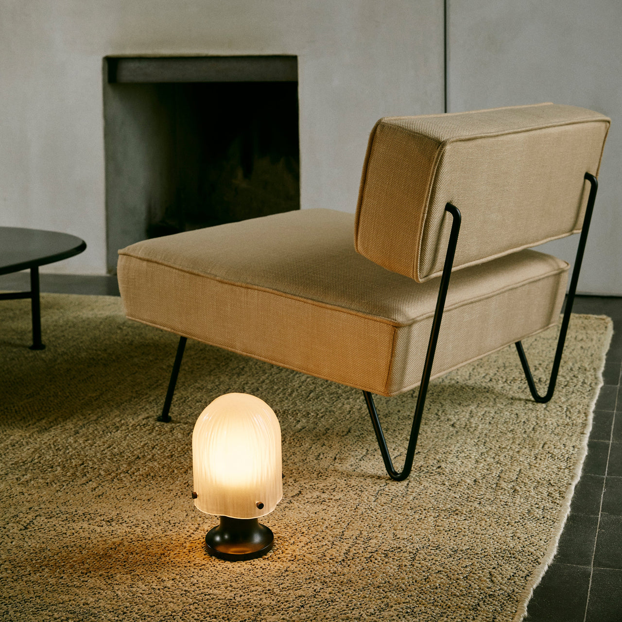 A glowing portable lamp with a ribbed frosted glass dome and dark base on a rug beside a tan chair