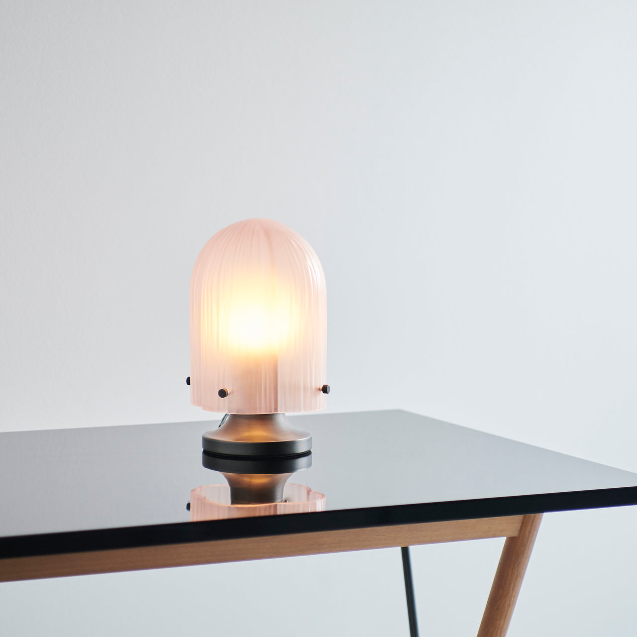 A glowing domed lamp with a ribbed pale pink glass shade on a metal base, on a glass-topped table