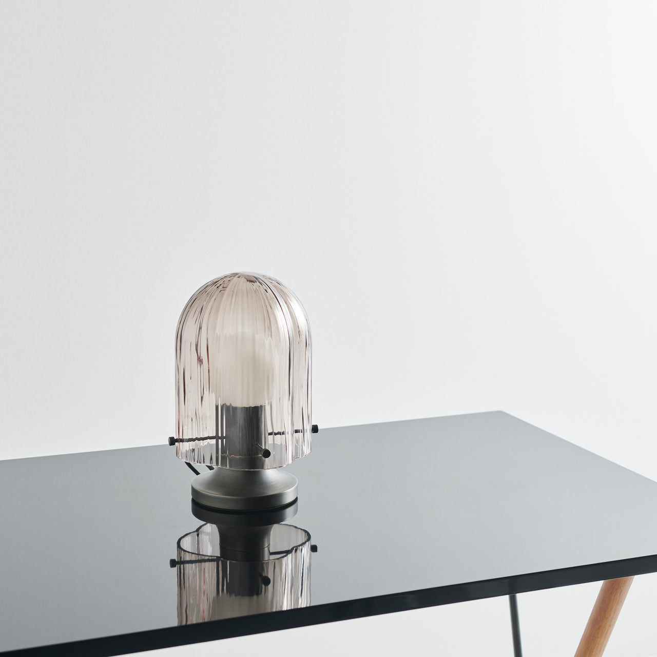 A dome-shaped table lamp with ribbed pale pink glass on a dark metal base, standing on a glossy black table