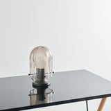 A dome-shaped table lamp with ribbed pale pink glass on a dark metal base, standing on a glossy black table