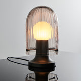 A lit table lamp with a ribbed smoky glass dome over a glowing bulb, on a dark metal base