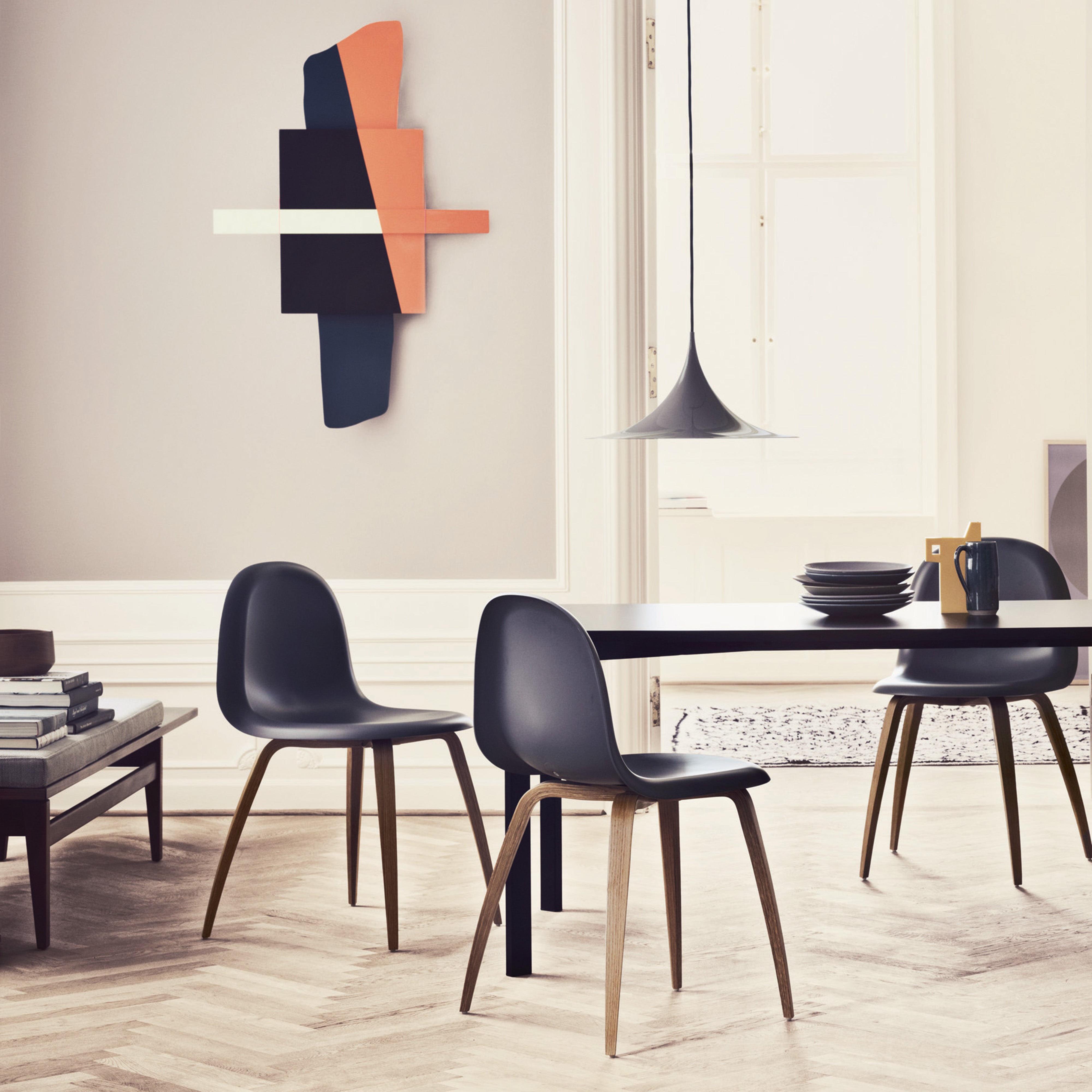 A dark grey cone-shaped pendant hangs over a black table with dark chairs on wooden legs