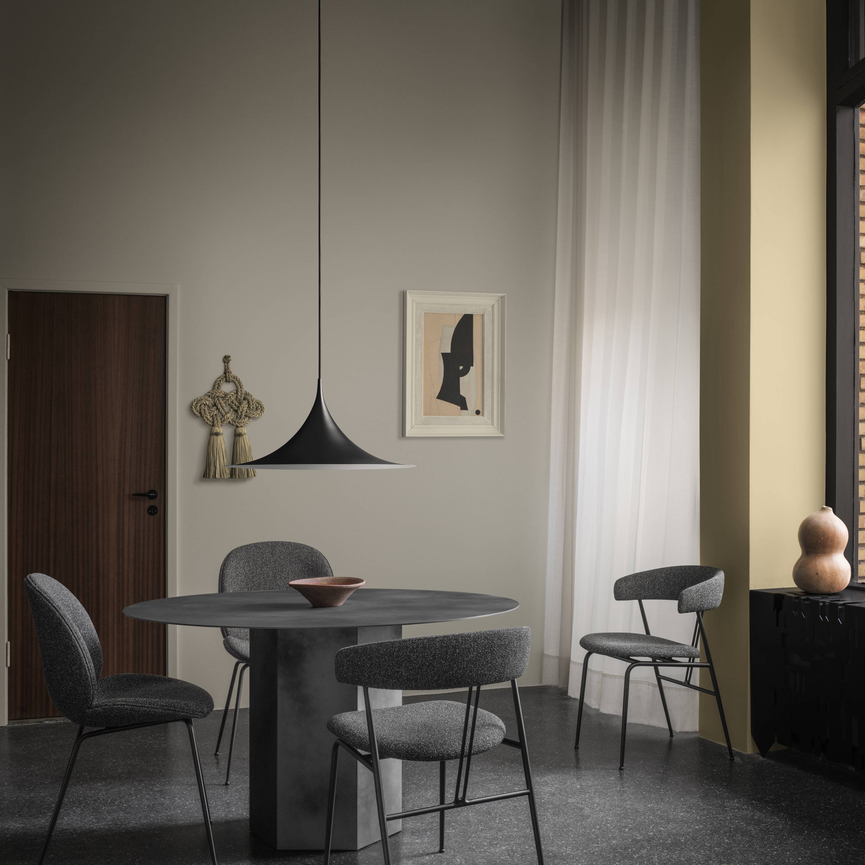 A black wide-brimmed pendant light hangs over a round dark grey table with grey upholstered chairs