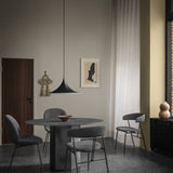 A black wide-brimmed pendant light hangs over a round dark grey table with grey upholstered chairs