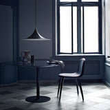 A wide black conical pendant light hangs over a round dark table and chair in a blue-grey room