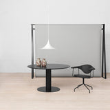 A white trumpet-shaped pendant hangs above a round black table, a black chair and a grey panel
