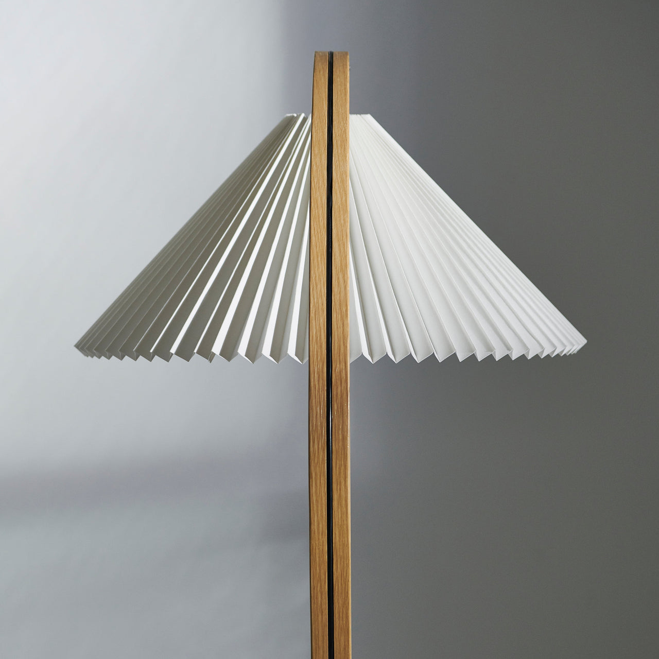 Close-up of a wide white pleated lampshade on a slim light oak pole with a dark centre seam