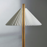 Close-up of a wide white pleated lampshade on a slim light oak pole with a dark centre seam