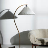 A floor lamp with a curved light wood arm and pleated white shade, casting shadows beside a cream sofa