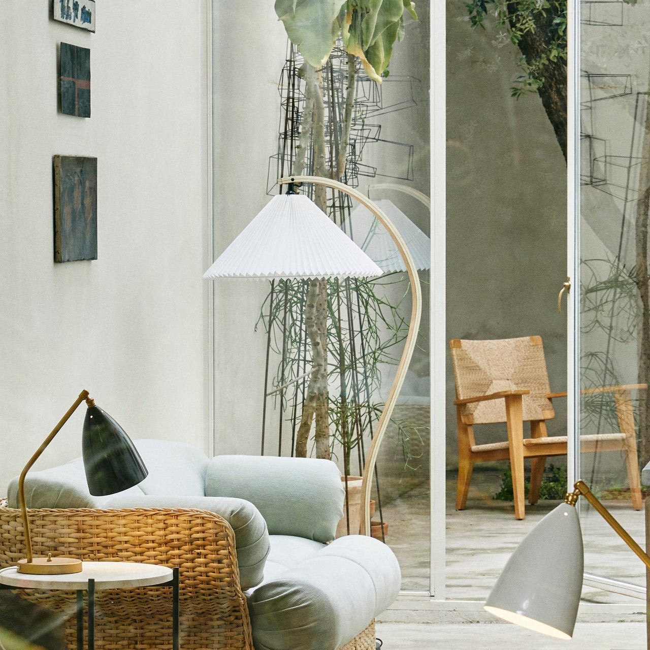 A floor lamp with a pleated white shade on a curved pale wood arm beside a rattan armchair