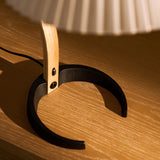 Close-up of a lamp's open black metal ring base and light wood stem on an oak surface