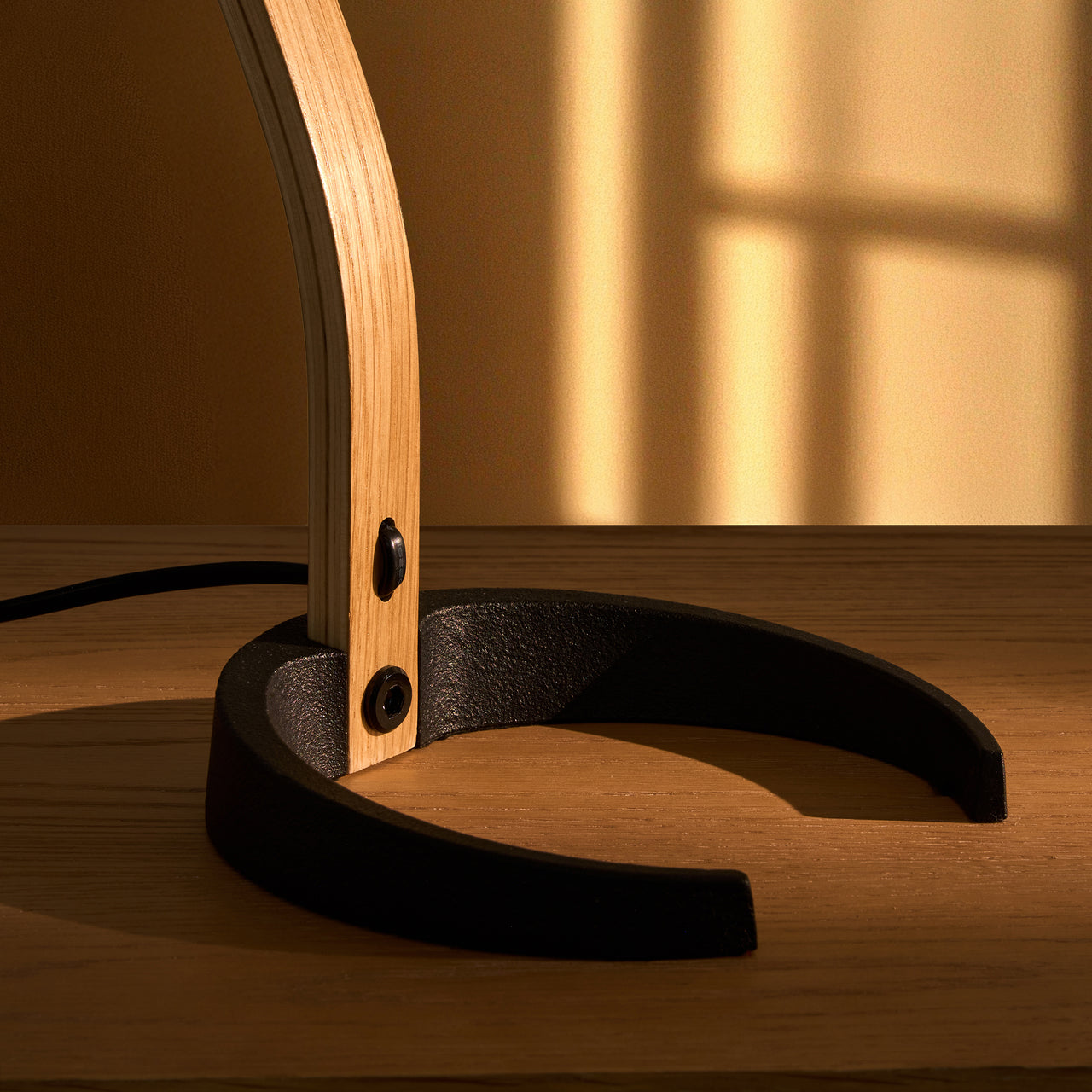 Close-up of a light wood lamp arm rising from a black horseshoe-shaped base on a wooden table