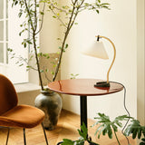 A table lamp with a pleated white shade and curved wooden arm on a round glossy red-brown table