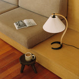 A table lamp with a pleated white shade and curved wooden arm on a built-in beige sofa platform