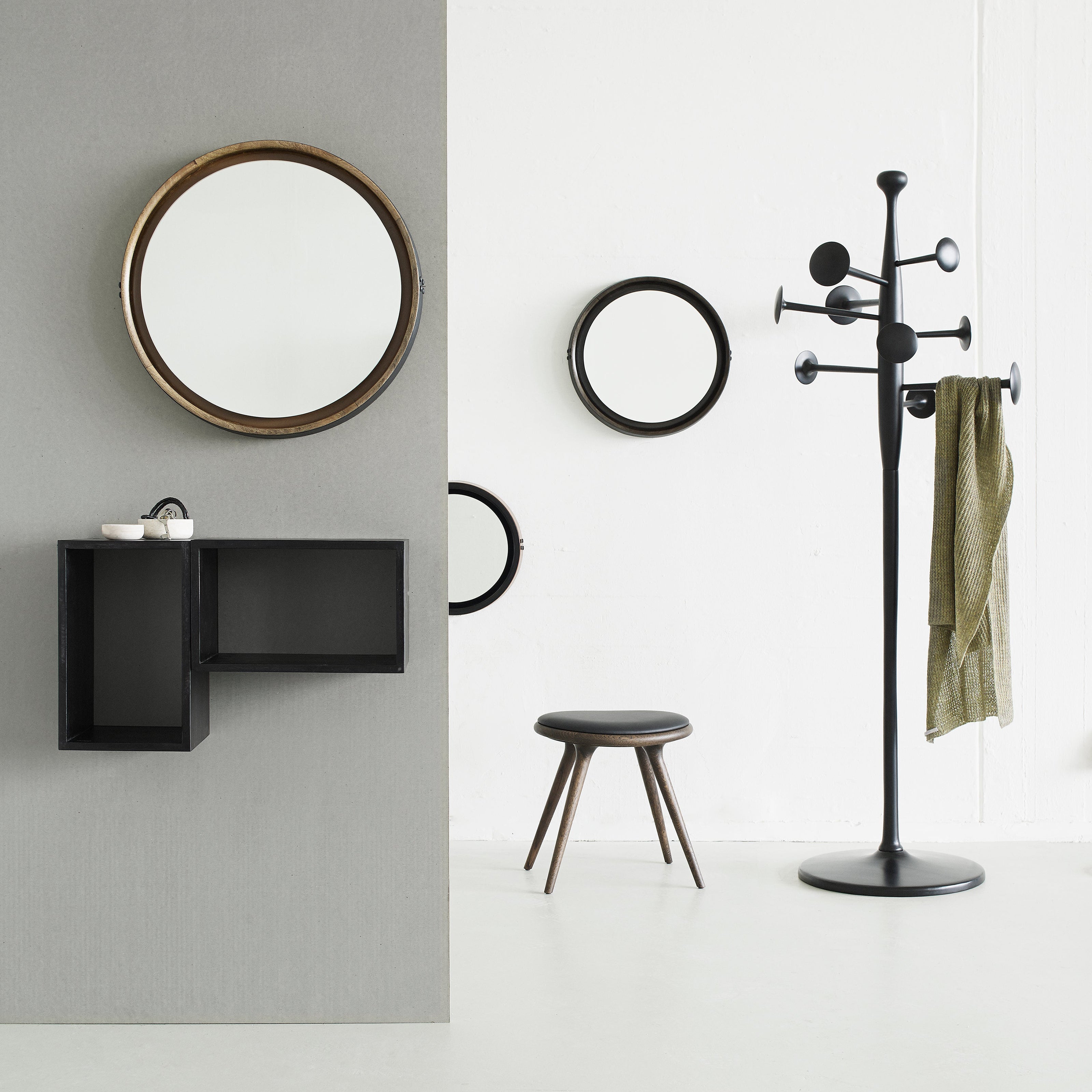 A black coat stand with disc-shaped hooks and a green scarf, beside round mirrors and a low stool