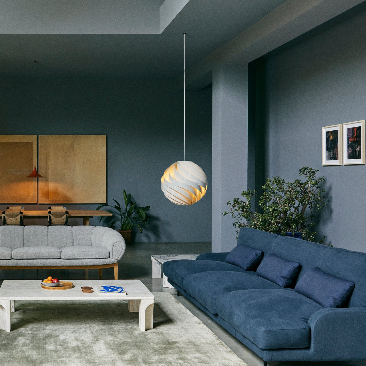 A white spherical pendant of overlapping twisted slats glows above a blue sofa in a grey-blue living room