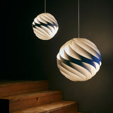 Two glowing spherical pendants made of twisting white slats, hanging beside wooden steps in a dark room
