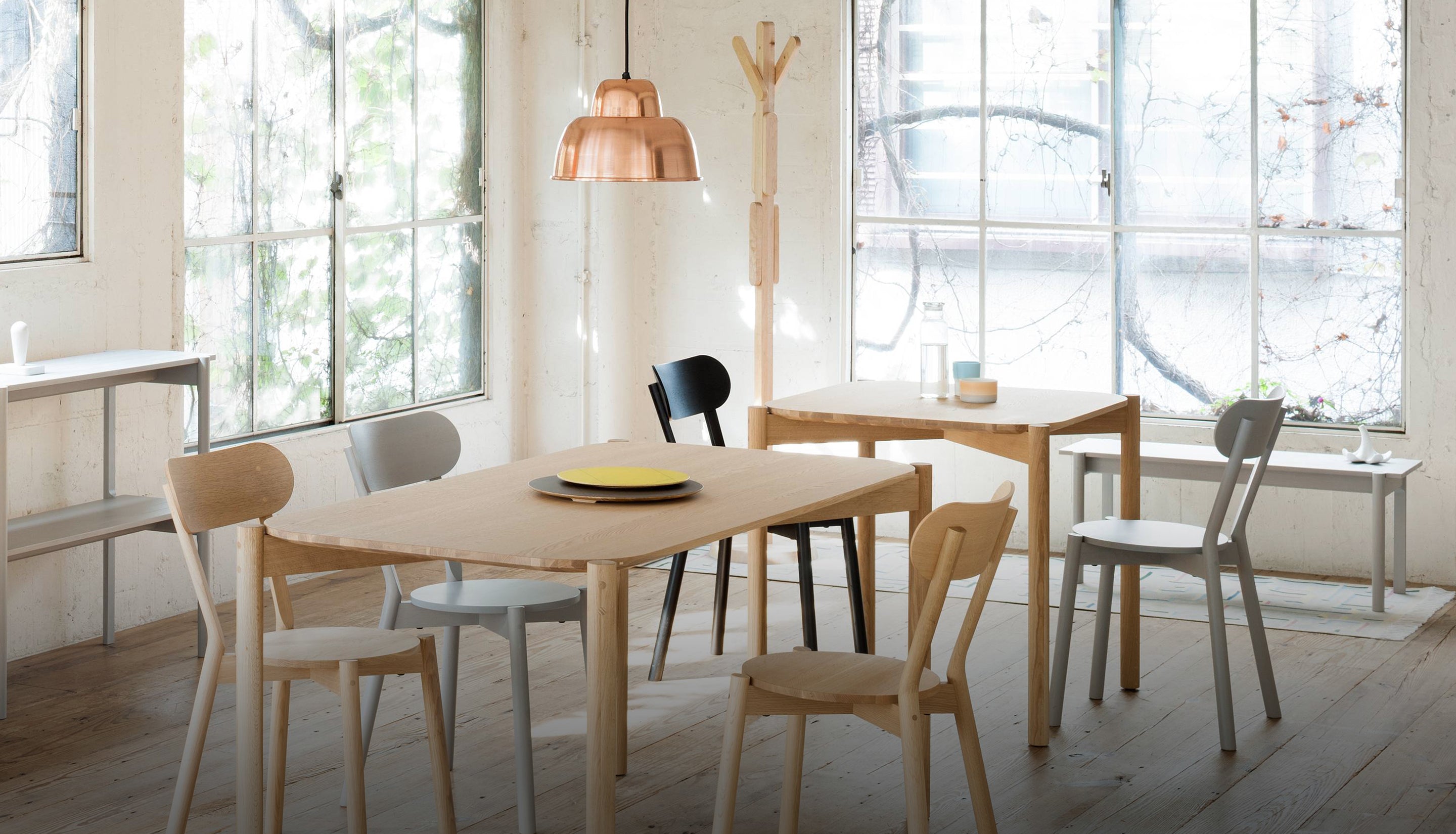 Dining area with wooden table and chairs in a bright room with large windows.