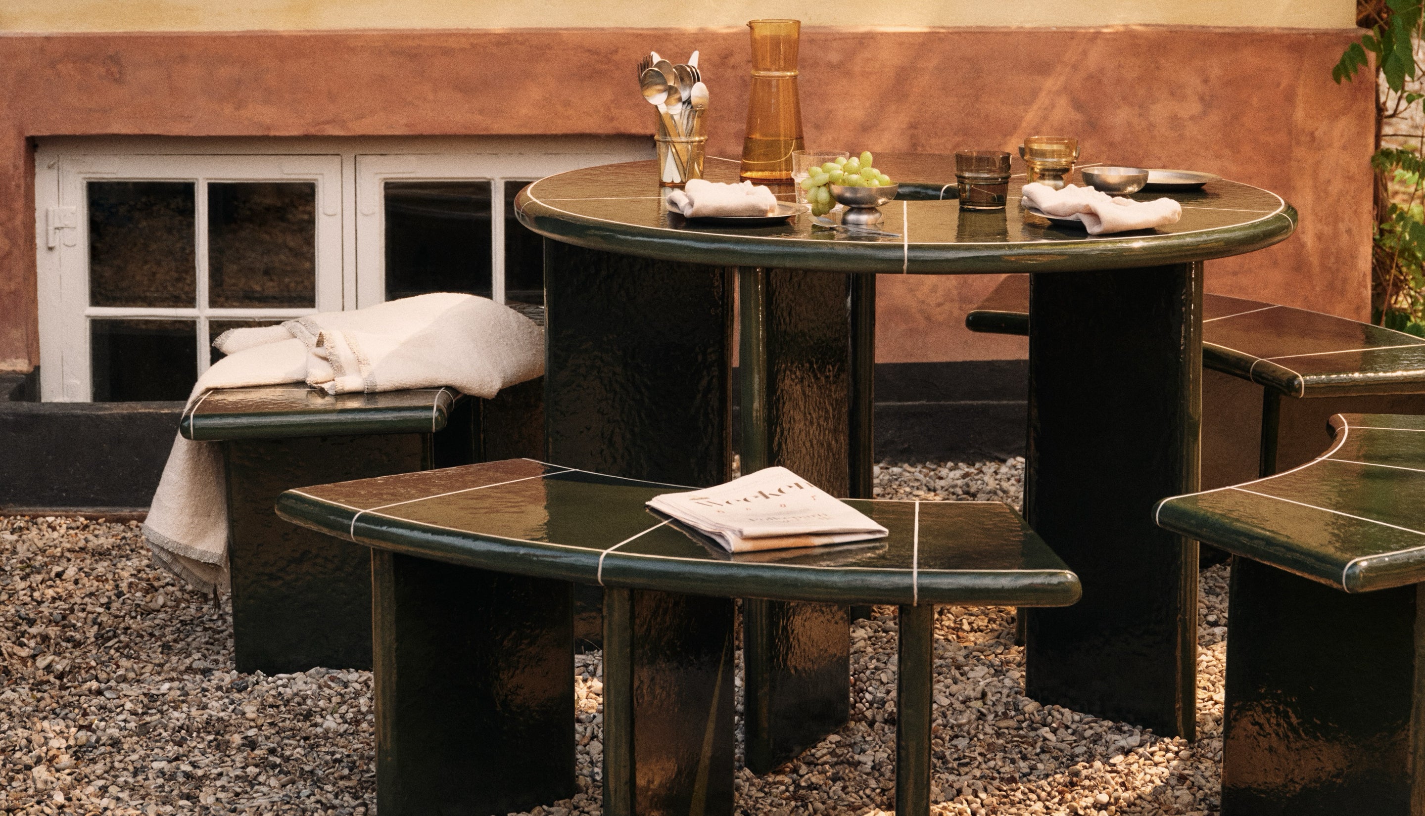 Ceramic tiled outdoor patio set in dark green on a pebbled floor outdoors.