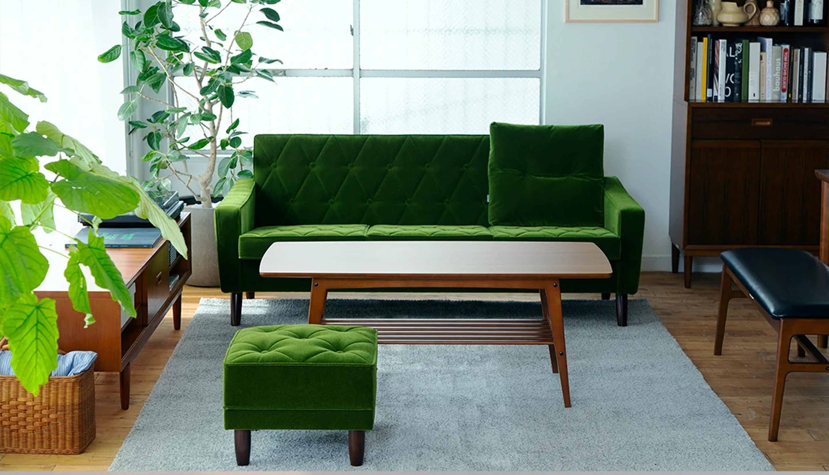 A livirng room scene where a green sofa and ottoman with wooden coffee table are the focal point.