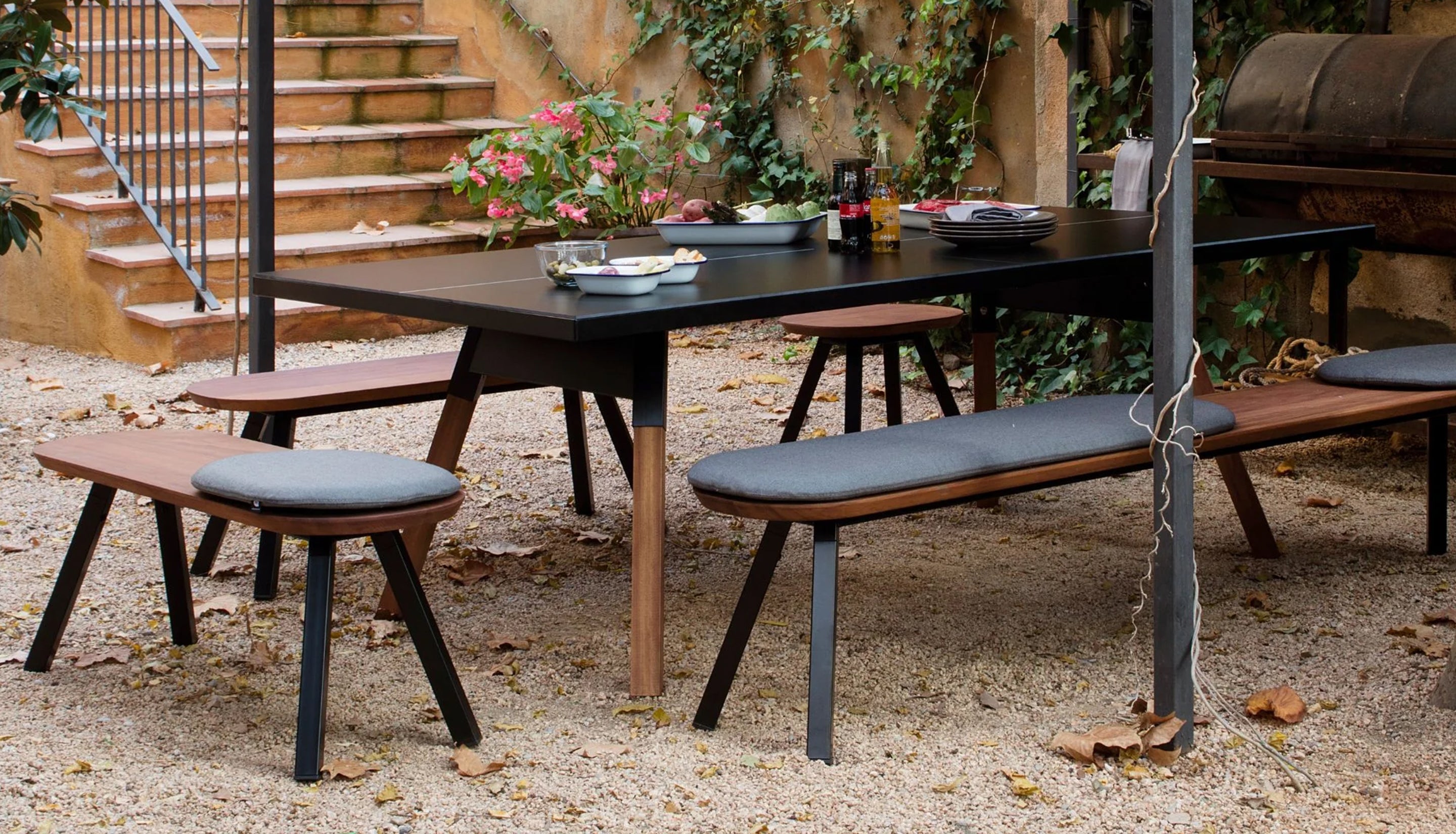 Outdoor dining setup with a table and benches in a garden setting.