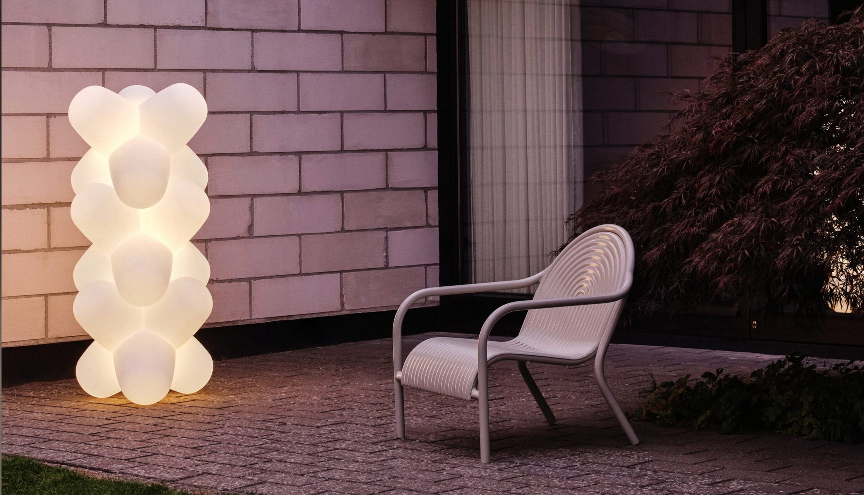 Outdoor setting with a modern chair and bubble-like lamp against a brick wall.