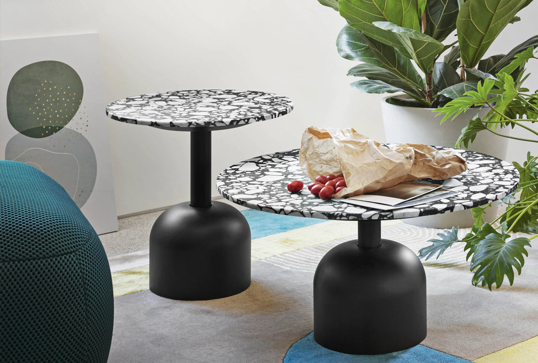 Modern black and white side table with a plant and bag of fruit in a room.