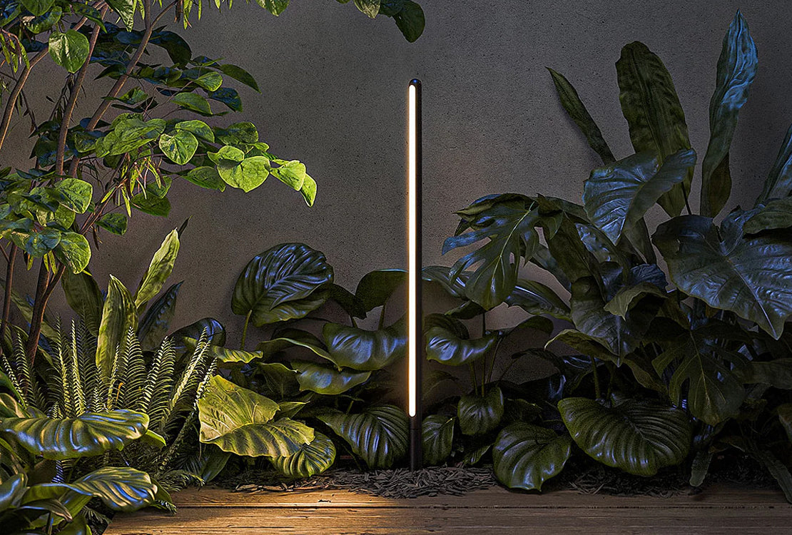 Modern outdoor light fixture surrounded by green plants on a wooden surface.