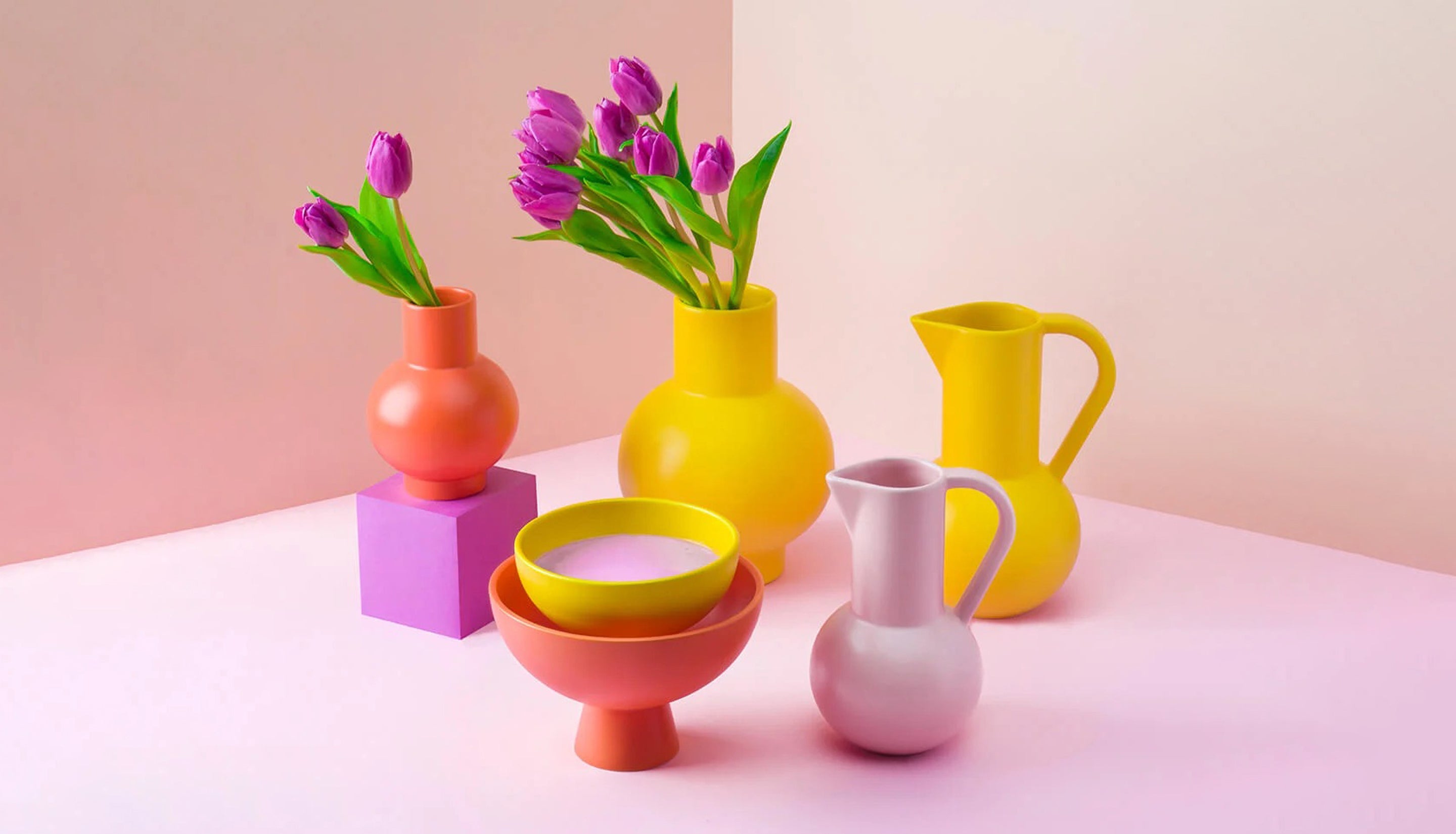Colorful ceramic vases and bowls with tulips on a light pink background