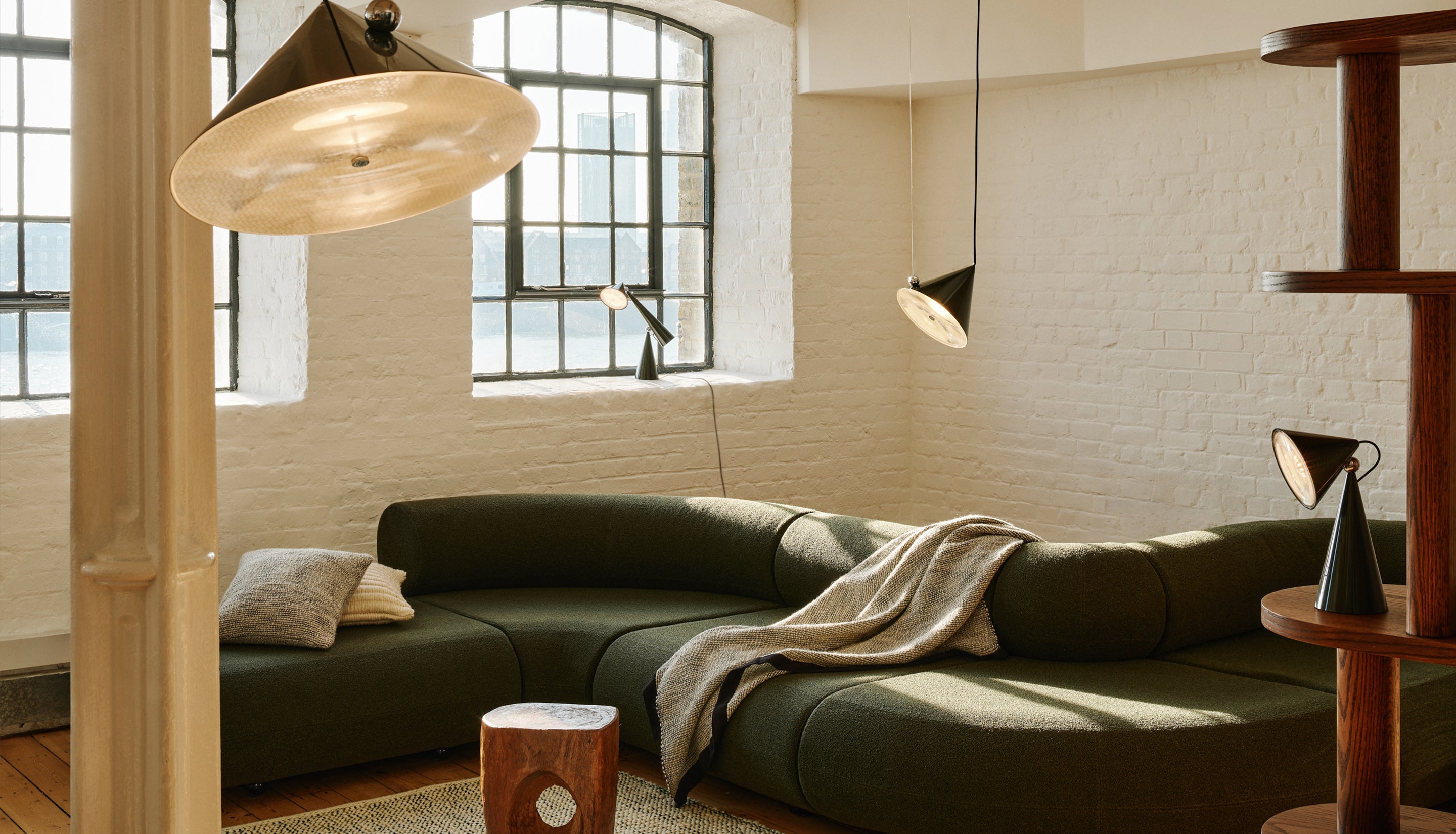 Modern living room with a green sofa, wooden side table, and pendant lights.