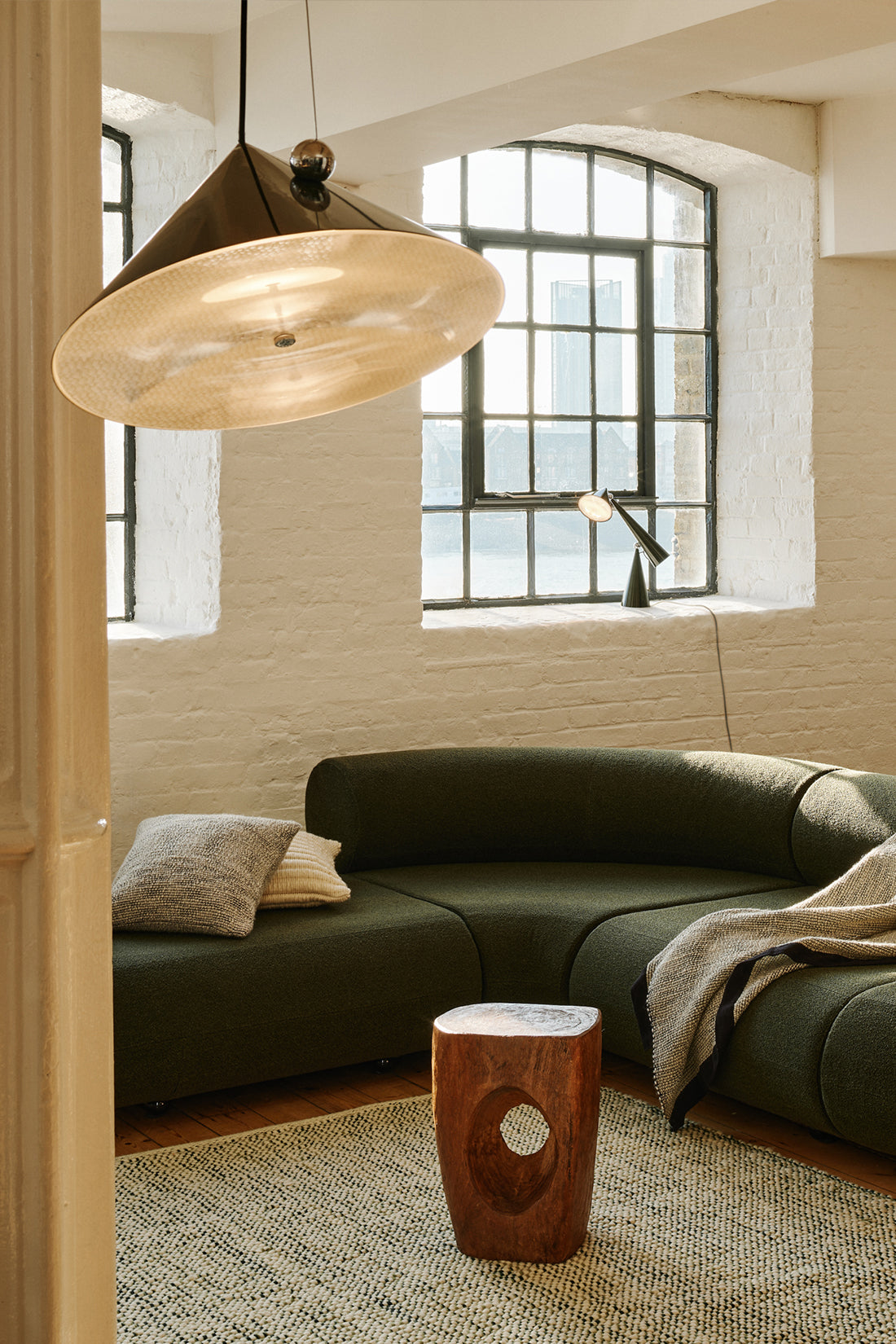 Modern living room with a green sofa, wooden side table, and large pendant light.